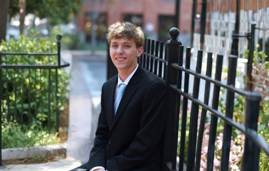 A smiling Brian Allen is dressed in a dark suit and seated outside.