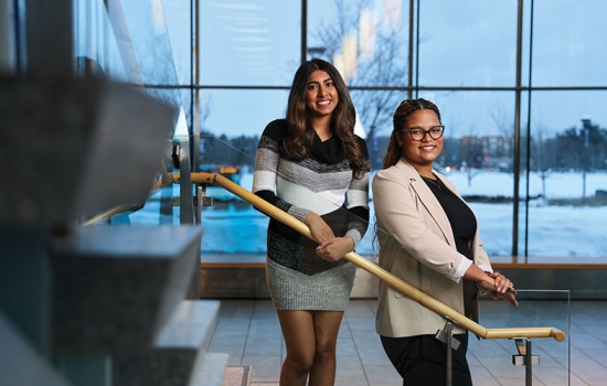Two scholarship recipients stand on the stairs in the Massry School of Business building