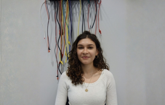 A smiling Marianna Karagiannas stands in front of a white wall adorned with dangling electrical cords. 