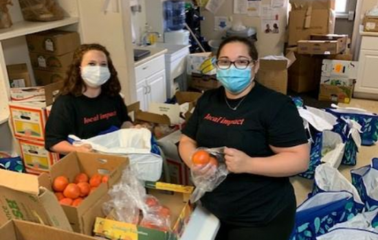 Elizabeth and a coworker bag oranges into plastic bags. They are wearing face masks.