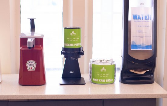 Condiments lined up on a counter include organic pepper and organic sugar, both with green Fair Trade labels