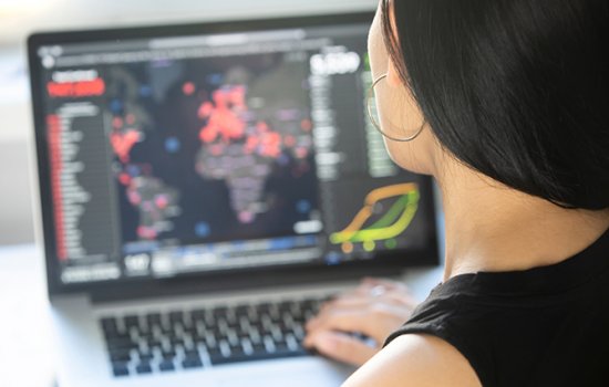 A woman looks at a screen showing a map of the world, where countries are dotted with red circles to indicate outbreaks of COVID-19 infection.
