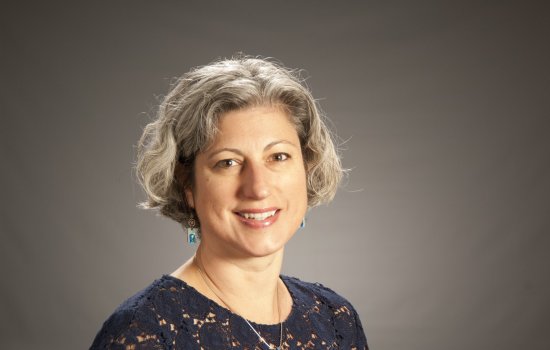 Dr. Janine Jurkowski smiles at the camera, standing against a grey backdrop.