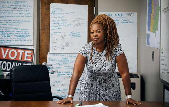 LaTosha Brown stands, leaning on her desk, surrounded by whiteboards covered in writing