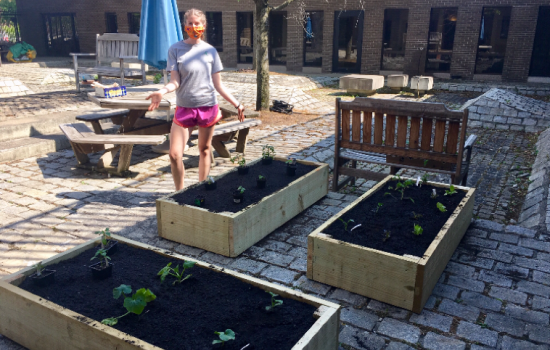 Leanna stands next to three wooden plant beds she has just created. They are outside on a brick patio, filled with dirt.