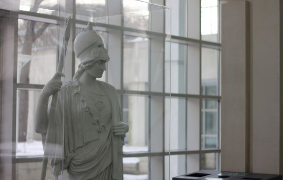 A statue of Minerva stands in the Science Library atrium. Glass windows are behind her.