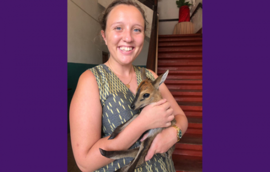 Alyssa smiles at the camera. She is indoors holding a baby kangaroo.