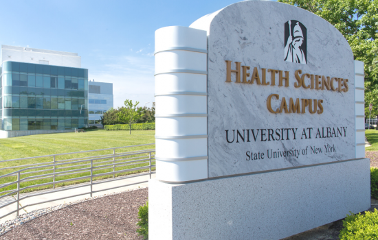 "Health Sciences campus" sign with a health science building, a blue sky, and bright green grass in the background.