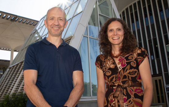 Drs. Yucel and Friedman stand smiling at the camera on the main UAlbany campus with glass architecture in the background.