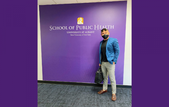Man smiling at the camera, standing in from of the School of Public Health sign.