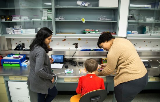 Two women help with tests in a clinical lab, working with a child.