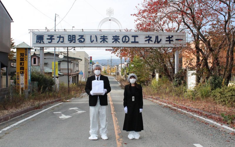 Yuji Onuma and his wife, Serina hold the ashes of his aunt in front of a sign in Fukushima that reads "Atomic power: Energy for a bright future."