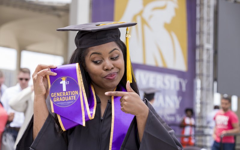 New graduate enthusiastically points at her first generation badge during UAlbany's undergraduate commencement ceremony.