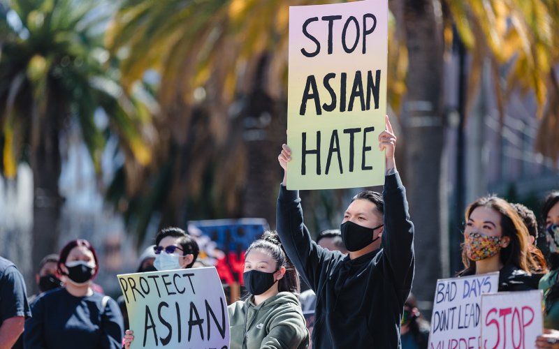 A young man holds up a Stop Asian Hate sign amidst a crowd of people holding similar signs below his