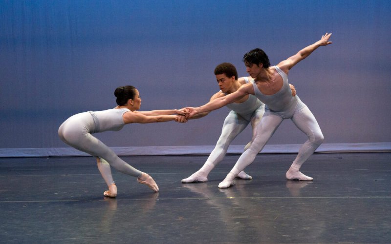 three dancers dressed in gray with two pulling against the other
