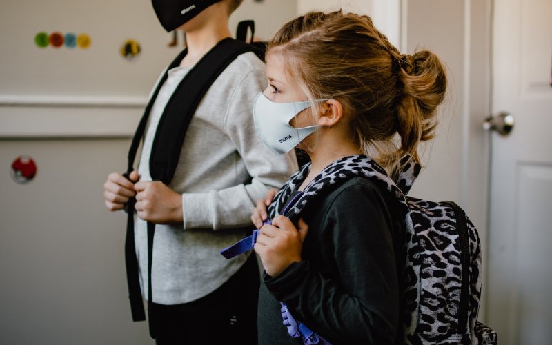 Two children side by side wearing masks with school backpacks.