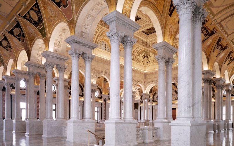 Interior view of the Library of Congress, with large white pillars and ornamental ceiling.