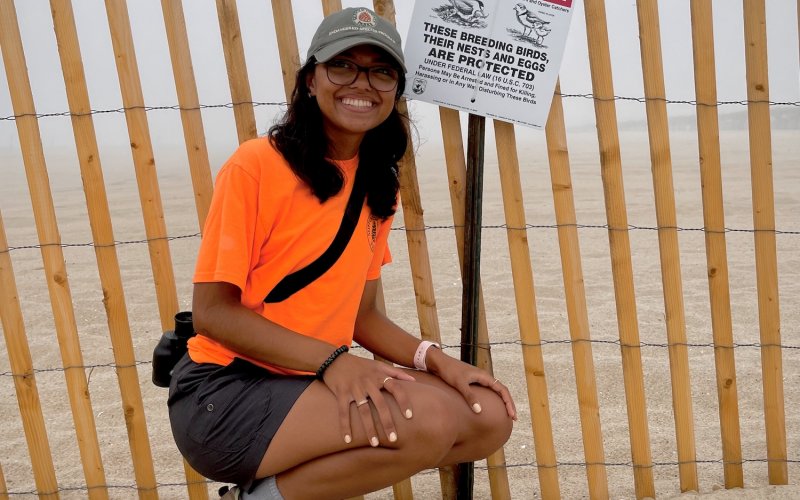 Student Mya Darsan crouches next to a fence affixed with a "Do Not Enter" sign, which explains that the bird nests and eggs in that area are a protected species. 