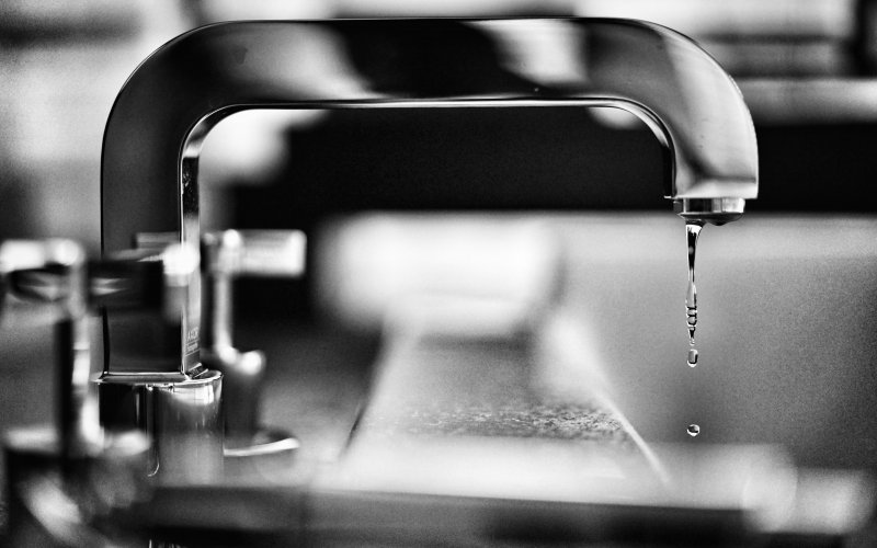 A kitchen faucet drips a little bit of water. The picture is in black and white.