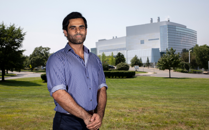 Ali Ropri stands outside the Cancer Research Center on the Health Sciences Campus. The green lawn is behind him.
