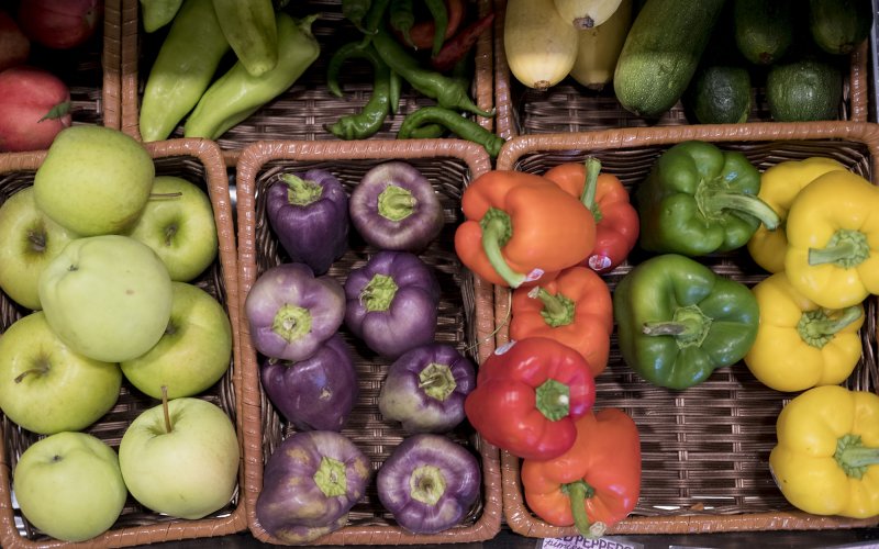 An overhead view of baskets filled with apples, peppers and cucumbers.
