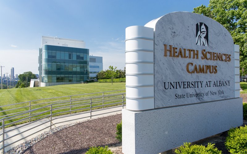 An exterior view of the Health Sciences campus, with the marble "Health Sciences Campus" sign in the foreground and the Cancer Research Center in the background.