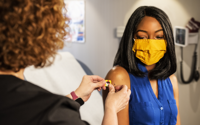 A woman wearing a yellow face mask receives a flu shot.