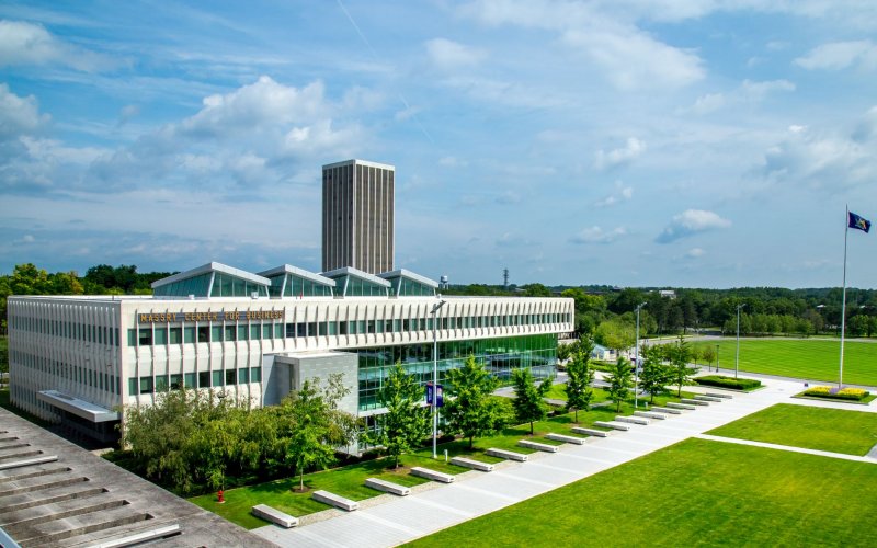 a modern cement and glass building with a row of trees and a green lawn