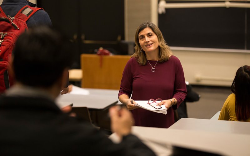 Candid photo of Professor Erin Bell teaching a class in a lecture center. Bell is smiling at a student. 