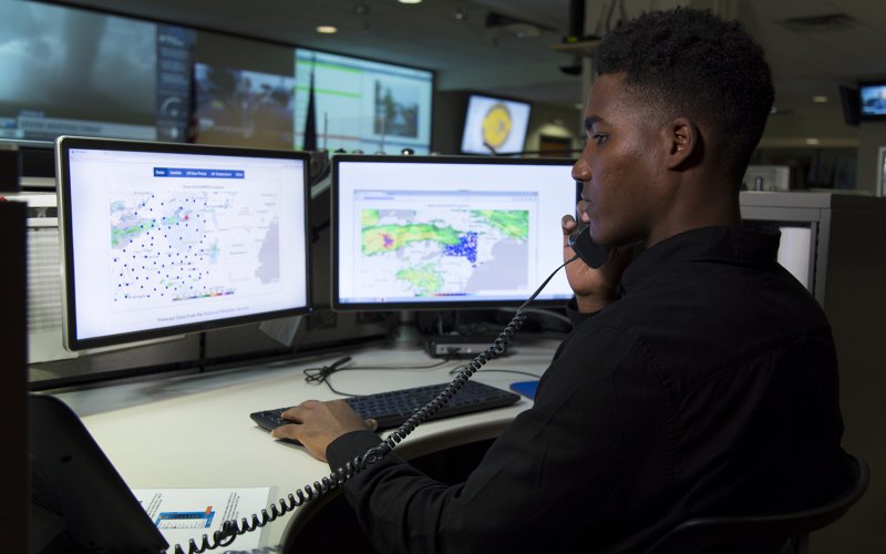A young African American man sits in front of two computer screens at the NYS Emergency Operations Center.