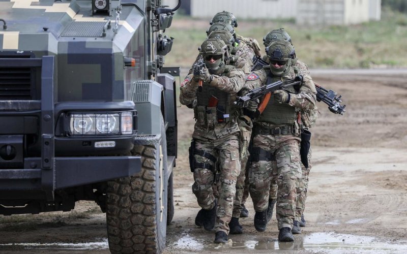 Ukraine military members armed with guns walk next to a transport vehicle on a muddy road during training in 2019.