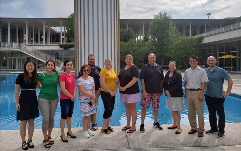 A group of 11 adult men and women stand in front of the main fountain pond.
