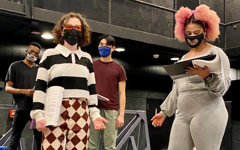 four individuals with scripts in hand rehearse a play