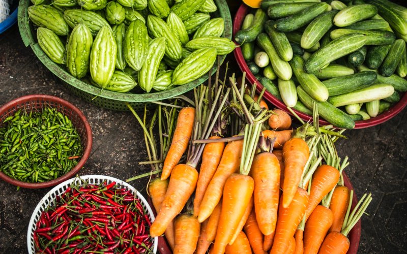 Produce vegetables sit in plastic baskets on a dirt floor.