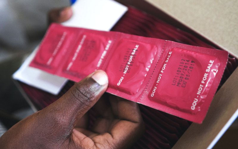 Closeup of a hand holding a strip of four condoms in red foil packets