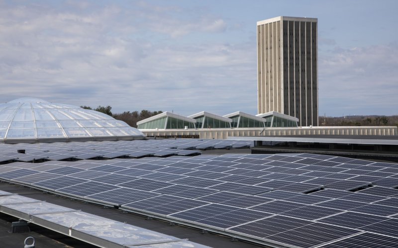 Solar panels cover a rooftop at UAlbany, with a residential tower in the background
