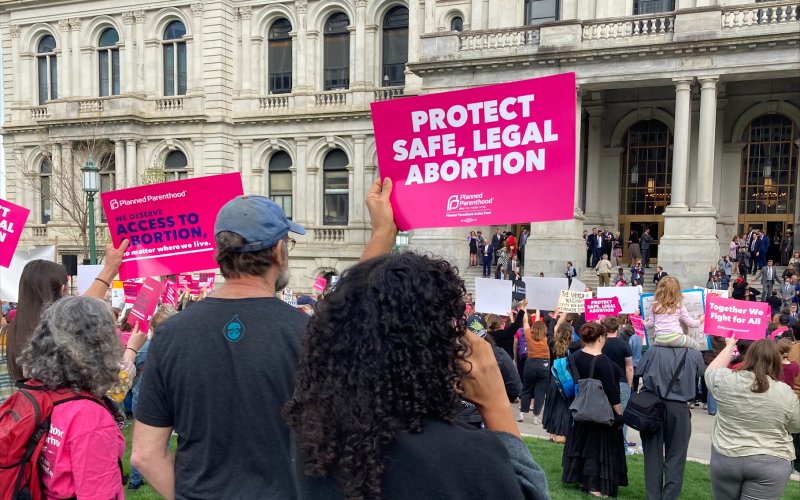 People holding up "protect Safe, Legal Abortion" and other signs at Abortion Rights rally outside the NYS Capitol building.