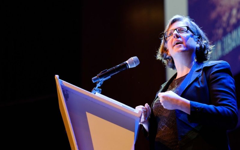 Virginia Eubanks, in glasses and a blue jacket, speaks at a microphone at a podium