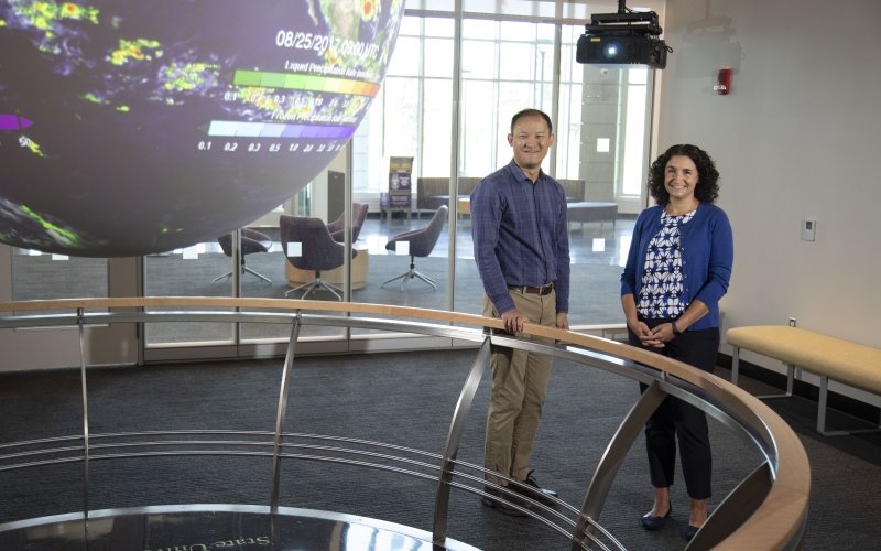 Professors Brian Tang and Kristen Corbosiero stand next to a globe display in the "Science On a Sphere" room at ETEC. 