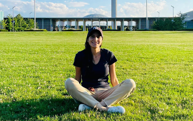 Maria Isabel Sanclemente sits on the grass in front of UAlbany's academic podium.