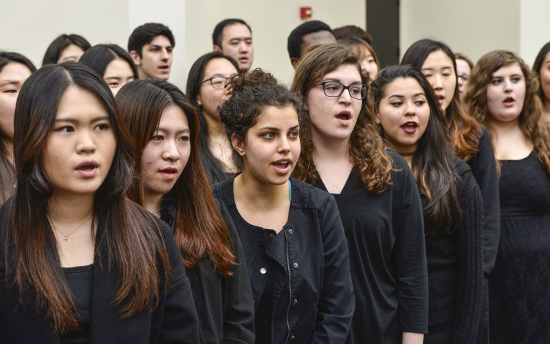 A group of singers dressed all in black stand in formation as they deliver a performance.