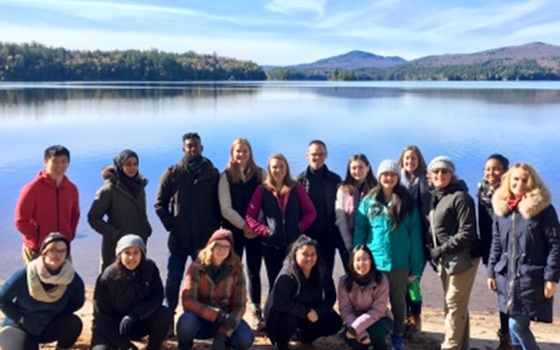 Public health students gather for a group photo in front a lake and Adirondack mountains