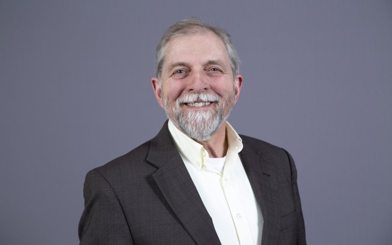 A smiling David Hoffman, with a white goatee, wearing a grey jacket and white shirt