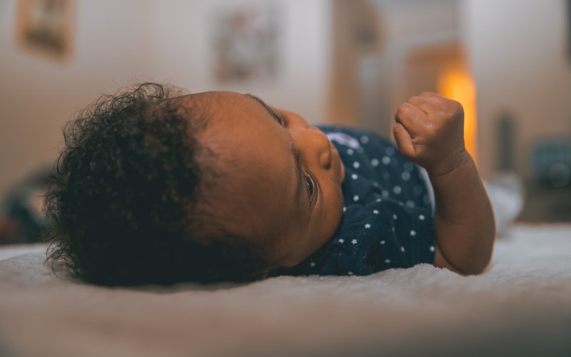 Baby wearing a dark shirt with star pattern reclines on a white, furry blanket. 