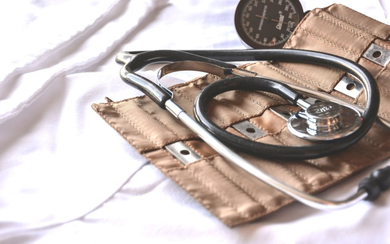 Black and silver stethoscope laid atop a brown blood pressure cuff. Instruments are arranged on a white cloth. 