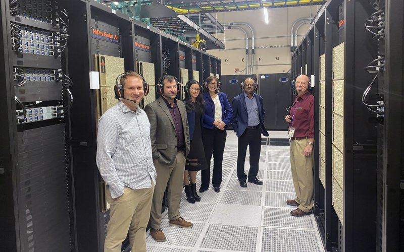 'A group of people stand in a supercomputer housing facility in front of servers that say "HiPerGator AI"