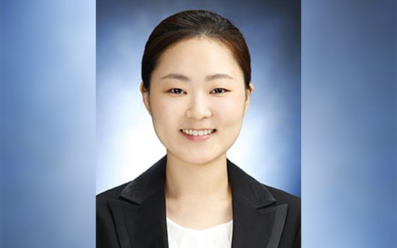 Kyoungah Noh smiles in a black blazer in front of a blue background