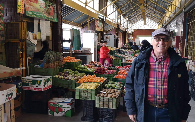 a man stands indoors in front of fresh fruit at a farmer's market in Santiago, Chile.