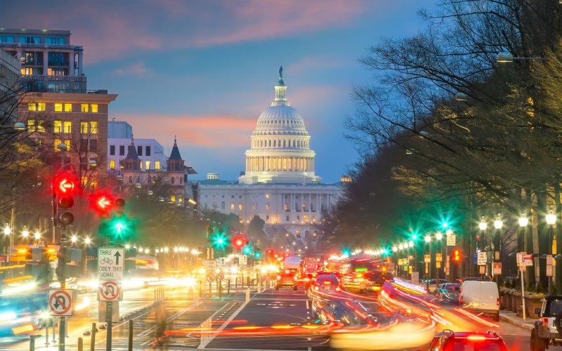 The U.S. Capitol building at dusk as cars with lights zoom by.