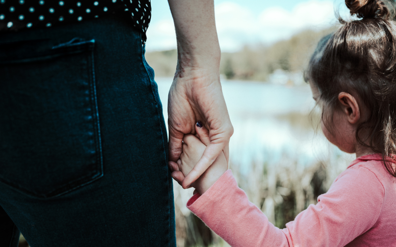 A woman holds a small child's hand.